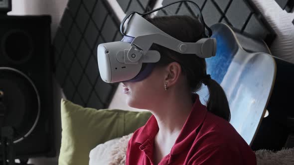 Young Woman in VR Helmet Sitting on Sofa and Communicating in Virtual World alt