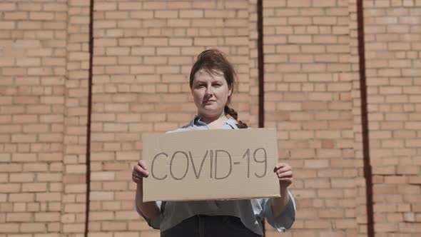 Portrait of Woman Holding Cardboard Sign COVID19 Monkeypox Near Brick Wall alt