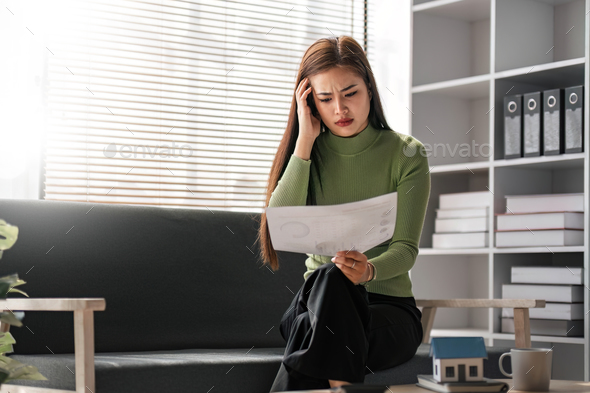 Serious and stressed Asian woman checking her monthly expenses bills in a living room.