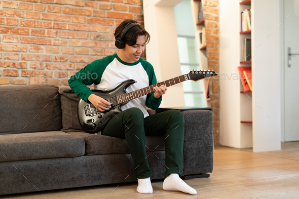Chinese Guy Learning Music Playing Electric Guitar Wearing Earphones Indoors