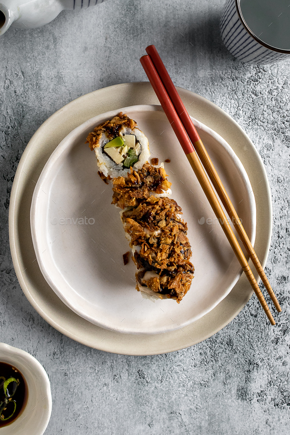 A crispy sushi roll on a white plate with chopsticks on neutral background - Stock Photo - Images