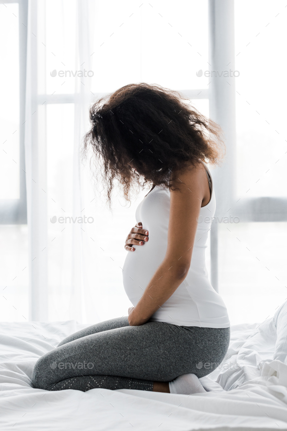 Curly Pregnant African American Woman Touching Belly While Sitting On