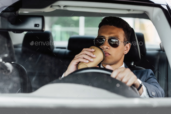 african american businessman in suit and sunglasses driving car and  drinking coffee at sunny day Stock Photo by LightFieldStudios