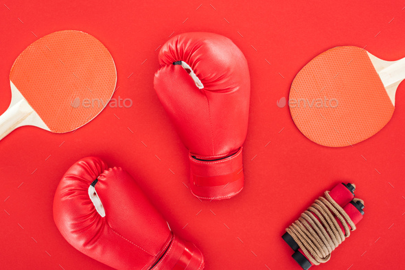 top view of boxing gloves near ping pong rackets near skipping rope isolated on red