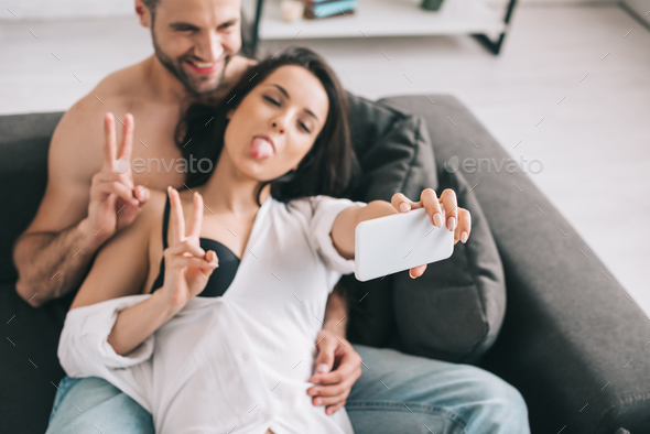 handsome man and sexy woman in shirt and bra showing victory sign and taking  selfie Stock Photo by LightFieldStudios