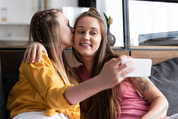 lesbian in yellow blouse kissing girlfriend while taking selfie