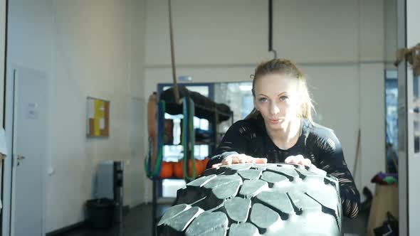 Caucasian athlete woman rolls big tires in the gym