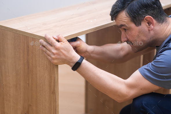 Furniture assembling services focused man in professional uniform assembling parts of shelf