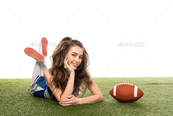 top view of sexy smiling cheerleader girl in blue uniform sitting with  pompoms on green field, Stock image