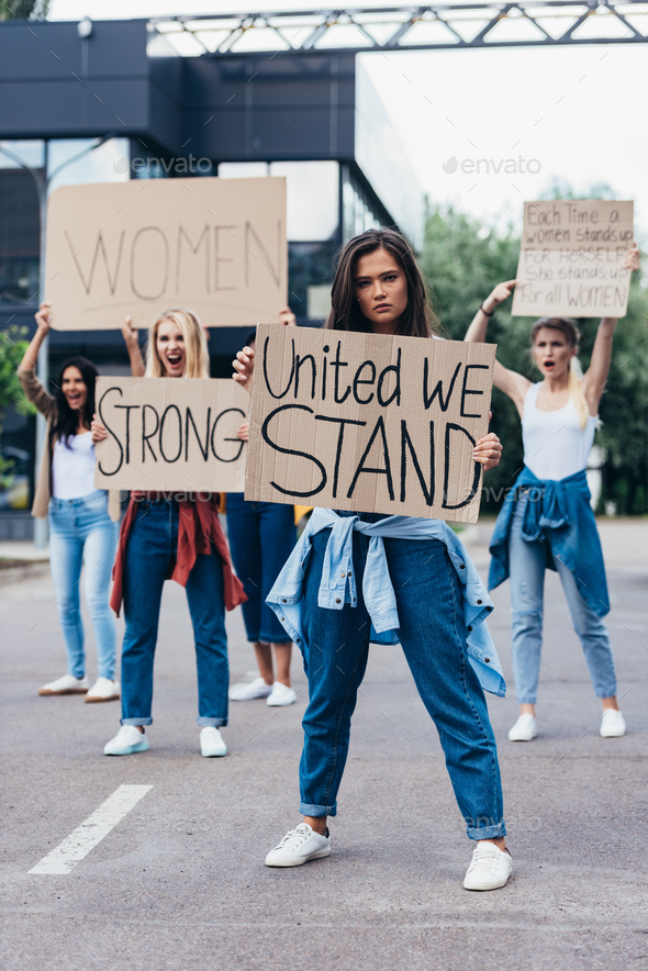 full length view of feminist holding placard with inscription united we stand near women on street
