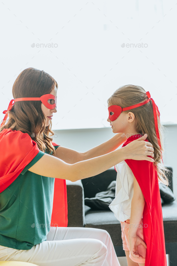 Mother And Daughter In Costumes Of Superheroes Looking At Each Other At