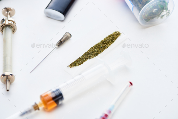 selective focus of syringes near rolling paper with marijuana on white background
