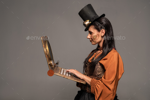 woman in top hat with goggles using steampunk laptop isolated on grey