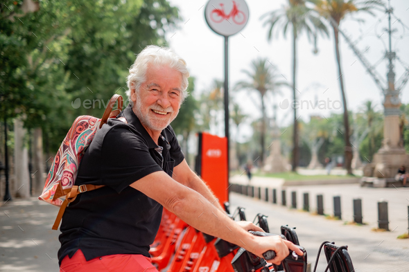 Happy senior man renting an electric city bike in Barcellona \'s park enjoying healthy lifestyle