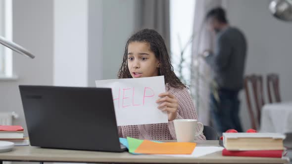 Portrait of Funny African American Schoolgirl Using Online Lesson on Laptop Showing Help Sign alt