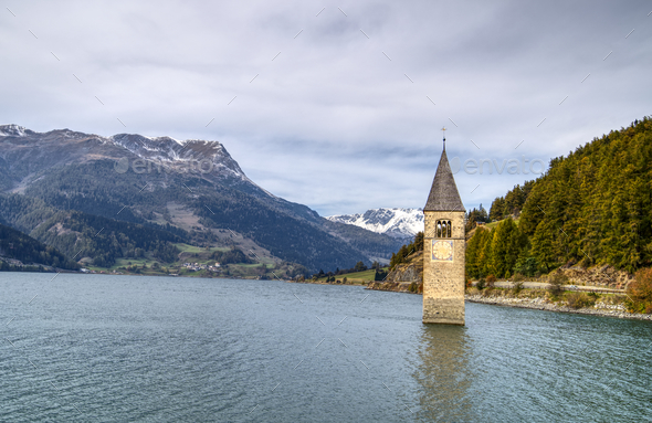 Submerged Clock Tower in the Reschensee surrounded by hills in South Tyrol, Italy - Stock Photo - Images