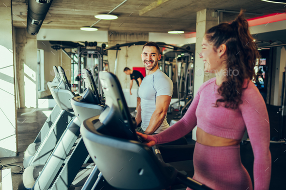 A happy sporty couple is preparing for running on a treadmill in a gym.
