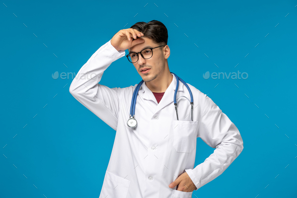 Doctors day cute young brunette guy in lab coat wearing glasses tired touching forehead