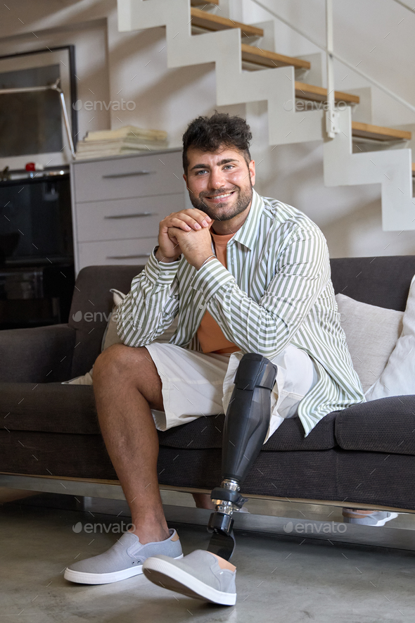 Happy amputee man with leg prosthesis sitting on sofa at home. Portrait