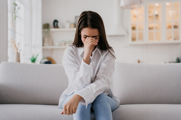 Upset girl sitting on sofa dressed in white shirt blue jeans, crying ...