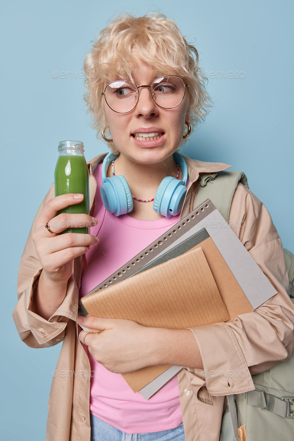 Worried female student attends language classes poses with notepads and bottle of fresh smoothie