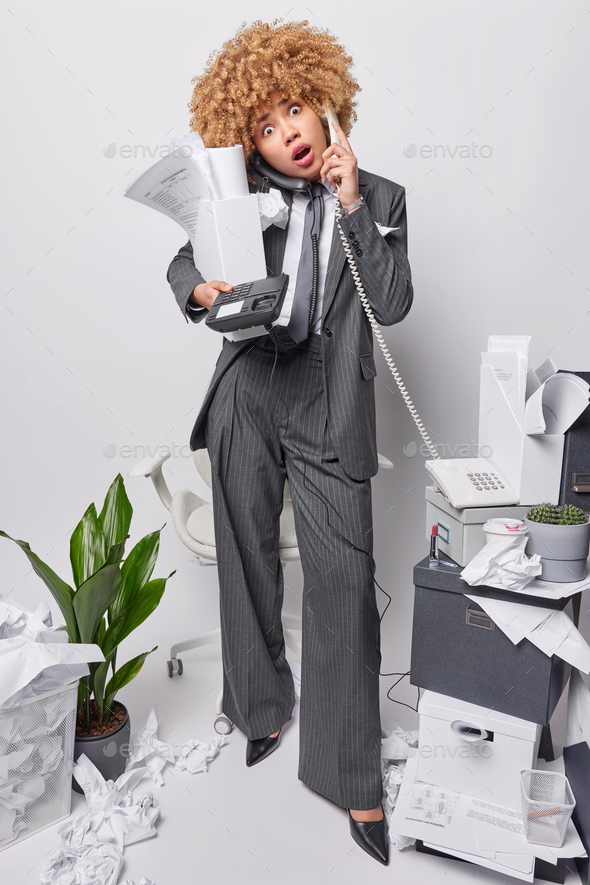 Multitasking female office worker or company employee answers client via stationary phone poses with