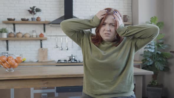 Portrait of Sad Overwhelmed Caucasian Woman Holding Head in Hands Looking at Camera alt