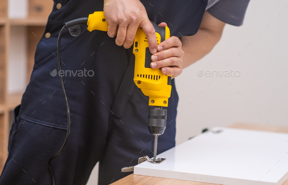 Furniture assembling skilled firm employee using electrical screwdriver on cabinet door fixing