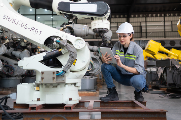 A female engineer installs a program on a robotics arm in a robot warehouse. - Stock Photo - Images