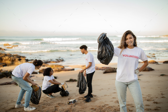 Positive proud young asian lady volunteer with friends in gloves show garbage bag, clean up trash