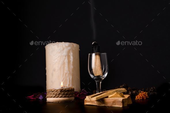 palo santo, holy stick smoking in a glass cup with lighted candles