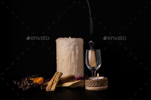 palo santo, holy stick smoking in a glass cup with lighted candles