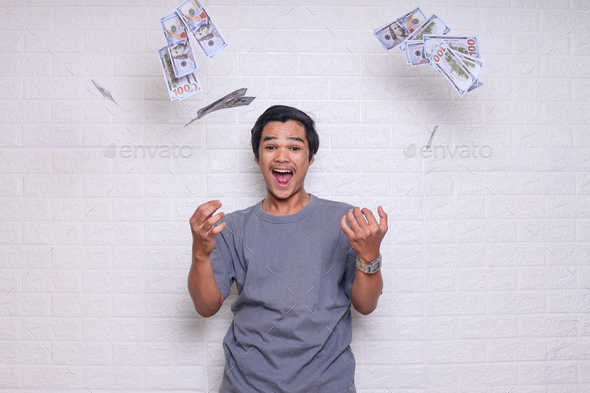 Attractive Asian man showing victory gesture under money fly rain