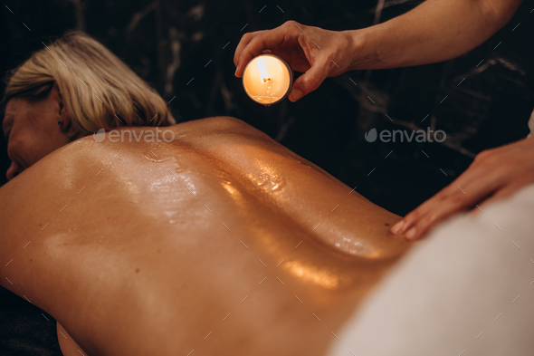 Masseur woman drips wax from a candle on the back of the young girl, rubbing massage oil.