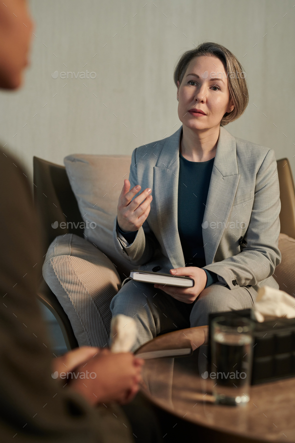 Confident mature female psychologist in formalwear looking at upset patient