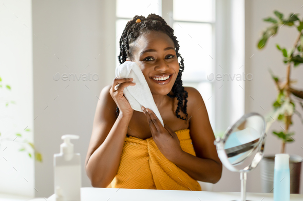 A moment of skin serenity. Happy black lady drying clean face with towel after shower, sitting in