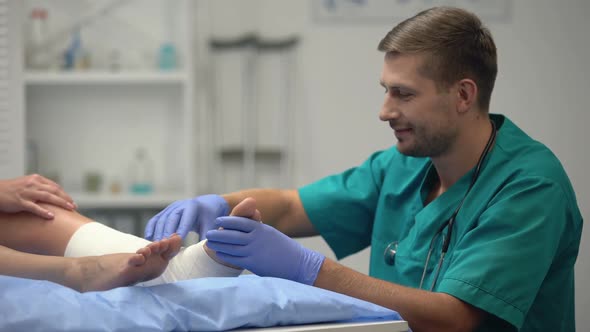 Attentive Doctor Checking Patients Elastic Wrap Leg, Talking Good Rehab Result