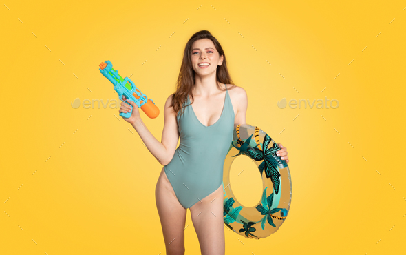 Portrait of young caucasian lady in stylish swimsuit posing with water gun and inflatable ring