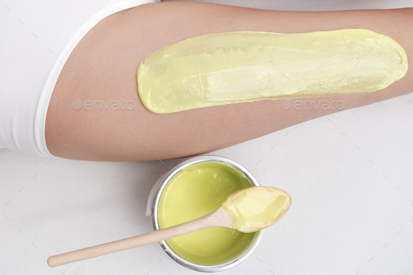 Cropped view from above of green hot wax on woman leg while she lying down on couch