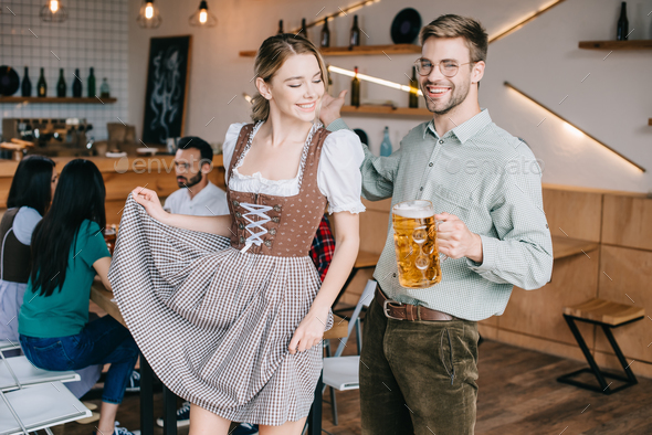 happy man and woman in traditional german costumes holding mugs of beer
