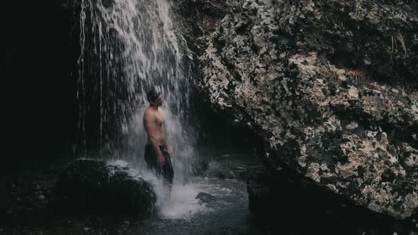 Young man in jeans standing under Niagara Waterfall on the river Cijevna in Podgorica, Montenegro alt