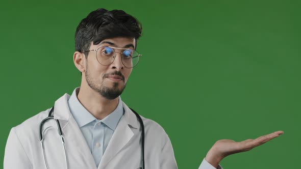 Arab Indian Guy Young Male Doctor Practitioner Man Hold Copy Space on Palm Pointing at Workspace alt