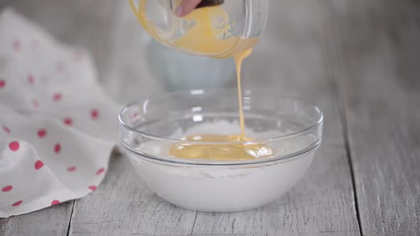 A Woman Adding Egg Yolks to Whipped Egg Whites a Mixing It with a Spatula in a Glass Bowl