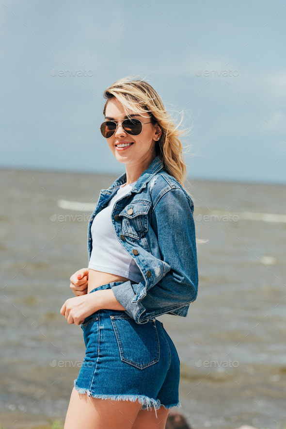 attractive woman in denim jacket and shorts looking at camera