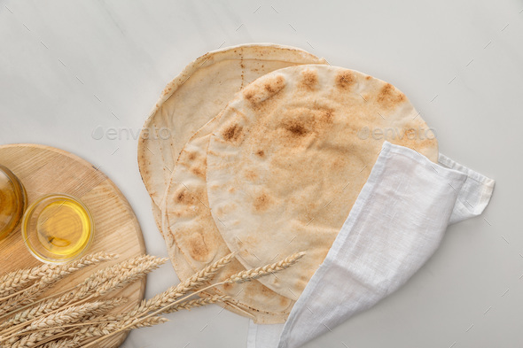 top view of flat lavash bread covered with white towel near cutting board with spikes and oil on