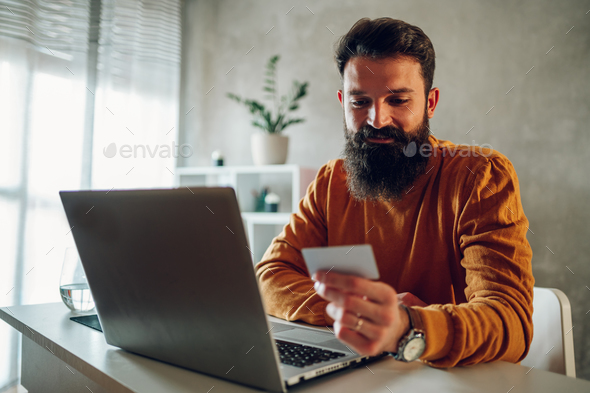 A happy hipster is paying online on an e-banking app his taxes and home bills while sitting at home.