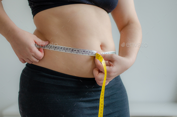 Slender woman measuring her waist with metric tape measure after a