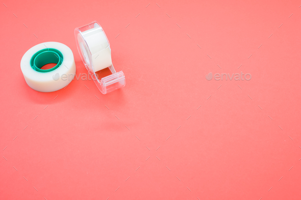 Top view closeup of a white duct tape and a tape dispenser isolated on a bright pink background
