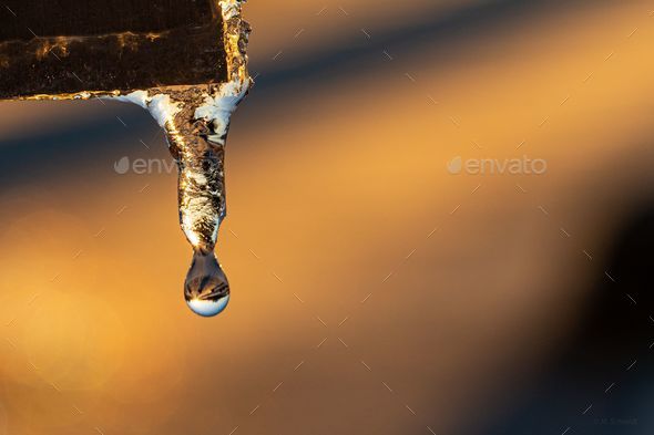 Close-up of a silver pipe with a melting icicle dripping from it
