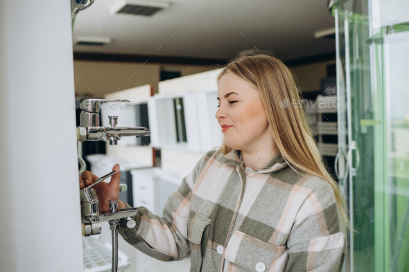 Smiling woman inspects and chooses new kitchen or bath tap faucet at a hardware store.